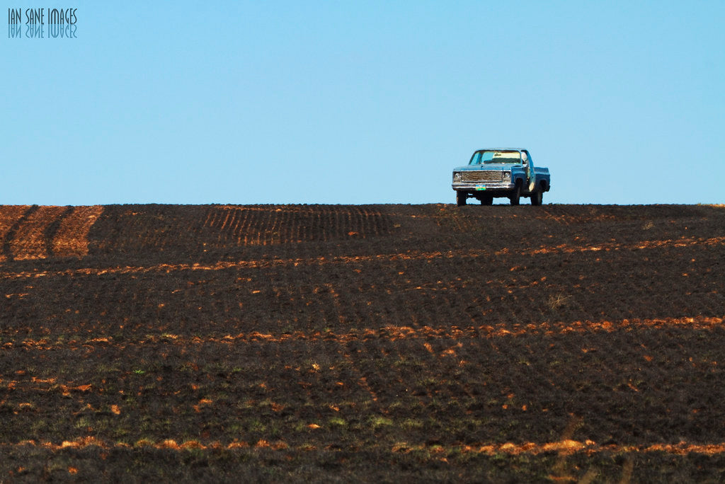 Pickup truck parked on the crest of a plowed field under a clear blue sky