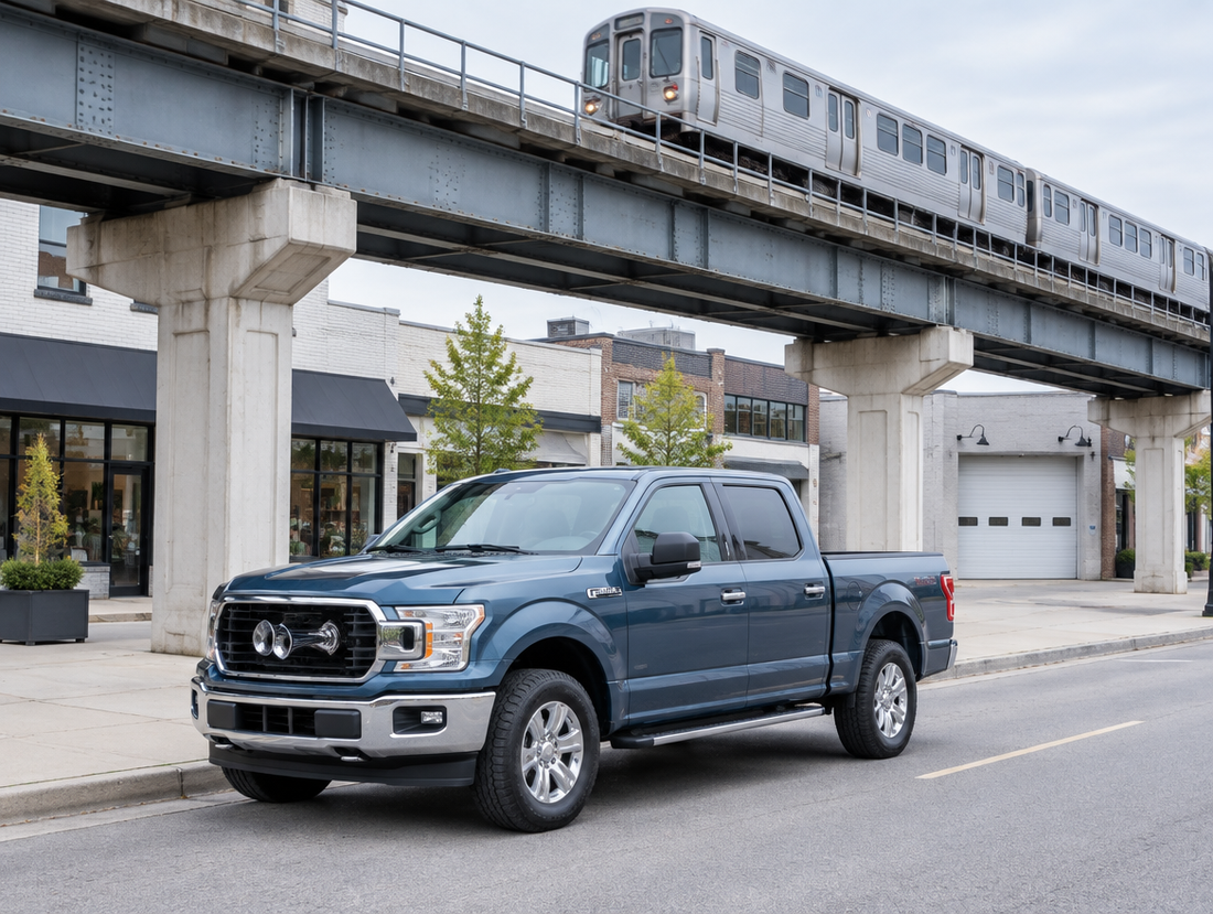 A clean pickup truck with a chrome air horn parked on a city street beneath an elevated rail viaduct.